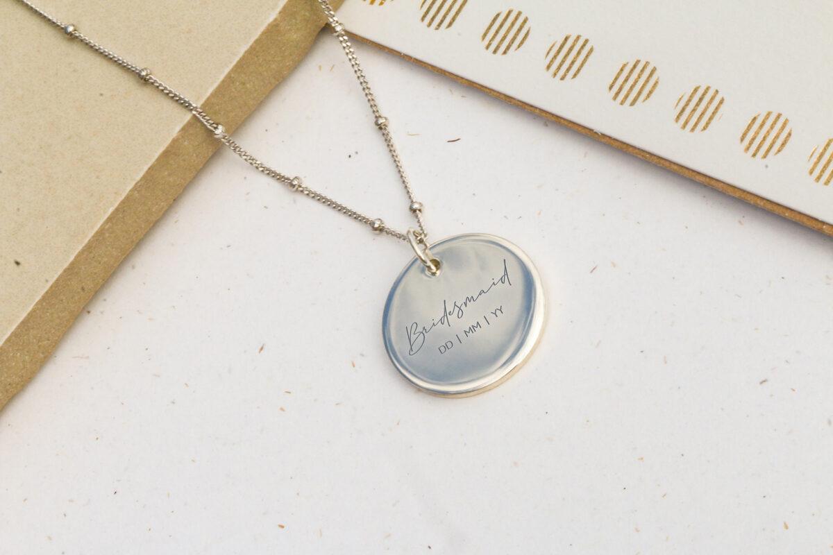 Image shows a Bridesmaid gift idea. A personalised silver pendant engraved with 'Bridesmaid' and the date of the wedding.